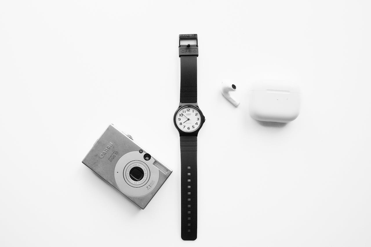 Black watch, camera, and earbuds arranged on a white background for a modern minimalist style.